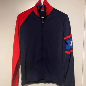 J.Lindeberg Tröja full zip - Grymt snygg J.Lindeberg tröja i blått med röda och blå detaljer. Perfekt för höst/vinter. Både för vardagligt bruk samt mer sportiga tillfällen. Tröjan har en hög krage och en dragkedja framtill. Den har även en J.Lindeberg-logga på vänster arm. Otroligt fina detaljer och är i magiskt bra skick. Storlek M men skulle säga att den mer sitter som S därav måste jag sälja (för liten på mig). Unisex. Skick 10/10. Som ny utan prislapp. ✨🔴🔵