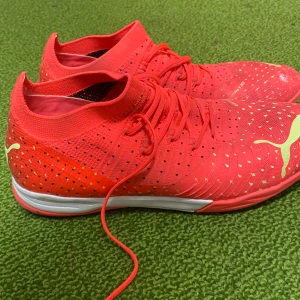 Röda fotbollsskor från Puma - Säljer ett par snygga röda fotbollsskor från Puma i mycket bra skick. Skorna har en tight passform med snörning och är perfekta för inomhusfotboll. De har en cool design med vita detaljer och Puma-loggan på sidan och hälen.