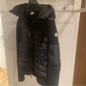 Svart jacka från Moncler - Säljer en snygg svart jacka från Moncler i mycket bra skick. Jackan har en quiltad design med dragkedja och en praktisk huva. Perfekt för höst och vinter, och den har en cool serietidningsetikett på insidan. Passar både till vardags och lite finare tillfällen. Köptes ifrån moncler hemsida, är riktig 
