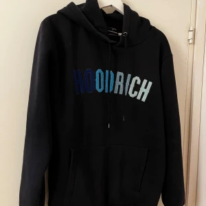 Svart hoodie från Hoodrich - Säljer en mörkblå hoodie från Hoodrich i bra skick. Den har en cool logga i blå och vit på framsidan. Perfekt för höst och vinter med sin mysiga känsla. Långärmad med en klassisk känguruficka och justerbar huva. Passar både till vardags och chillkvällar.