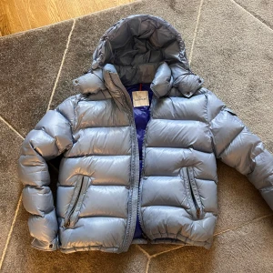 Ljusblå Moncler Maya - Säljer en snygg ljusblå dunjacka från Moncler i bra skick. Jag köpte jackan begagnad för 3 månader sedan, jag har använt den en del men inte jättemycket för det inte har varit så kallt så jag ville använda den. Den är mycket varm och skön! Den har lite små fläckar som man kan se på sista bilden, kemtvätt kan absolut ta bort dem. Jag säljer den ”billigt” för att jag som sagt köpte den begagnat och nu vill jag bara ha pengar, ska köpa bil så småningom ;)