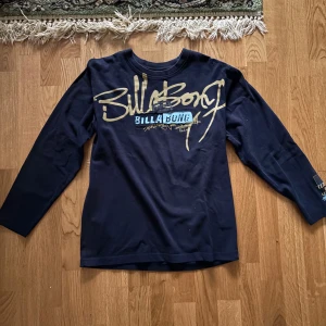 Mörkblå långärmad tröja från Billabong - Säljer en mörkblå långärmad tröja från Billabong med stort tryck i beige och blått på framsidan. Perfekt för en avslappnad stil. Tröjan har en rund halsringning och är tillverkad i ett mjukt material.