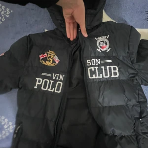 Svart pufferjacka från Vinson Polo Club - Säljer en svart pufferjacka från Vinson Polo Club med broderade detaljer och dragkedja. Jackan har en sportig look med tryck på bröstet och är perfekt för kyligare dagar.