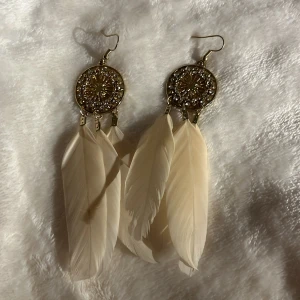 Örhängen med fjädrar - Örhängen med fjädrar. Oanvända. Dem runda ringarna är i metall.