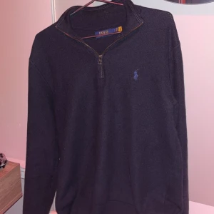 Mörkblå tröja från Polo Ralph Lauren - Säljer en stilren mörkblå tröja från Polo Ralph Lauren med dragkedja vid halsen. Tröjan har långa ärmar och är perfekt för en avslappnad look. Den ikoniska loggan är broderad på bröstet.