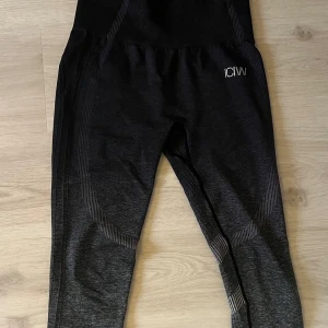 Svarta/grå tights från ICANIWILL - Snygga tights från ICANIWILL med hög midja och ribbade detaljer. Perfekta för träning med en tight passform som ger bra stöd. Diskret logga på sidan och stilrena mönster längs benen. Storlek S