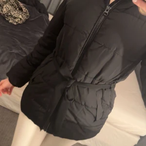 Svart dunjacka med dragkedja - Säljer en svart dunjacka med dragkedja och huva. Jackan har en normal passform och är perfekt för kyligare väder. Den har långa ärmar och praktiska fickor framtill. En stilren och funktionell jacka för vintern.