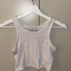 Vit ribbad linnetopp - Säljer en stilren vit ribbad linnetopp från lager 157. Perfekt för varma dagar med sin ärmlösa design och croppade längd. Enkel och snygg att matcha med olika outfits.