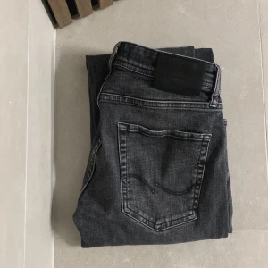 Svarta jeans från Jack & Jones - Snygga svarta jeans från Jack & Jones med en klassisk femficksdesign. De har en knappgylf och är tillverkade i ett slitstarkt denimtyg. Skick 8,5/10 i modellen ”Mike”