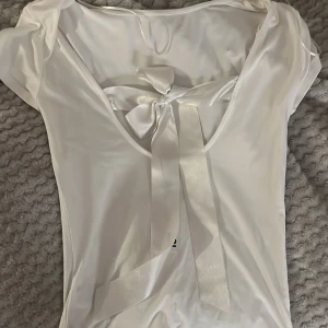 Vit topp med rosett - Säljer en stilren vit topp med korta ärmar och en vacker rosett.och är tillverkad i ett mjukt material som ger en skön passform. Perfekt för att ge en touch av elegans till din outfit.har aldrig använts 