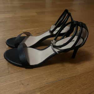 Svarta sandaler från Graceland - Eleganta svarta sandaler från Graceland med smala remmar och klack. Perfekta för en stilren look. Sandalerna har en öppen tå och justerbar rem runt ankeln.