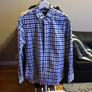 Blå och vit rutig skjorta från Ralph Lauren - Snygg blå och vit rutig skjorta från Ralph Lauren i slim fit. Skjortan har långa ärmar och knappar framtill. Den är broderad med det klassiska Ralph Lauren-märket på bröstet. Perfekt för en stilren look! skriv gärna vid frågor! Skjortan är som ny inga defekter! Kan gå ner i pris vid snabb affär.