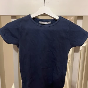 Mörkblå ribbad t-shirt från Lager 157 - Säljer en stilren mörkblå ribbad t-shirt från Lager 157. Den har en klassisk rund hals och korta ärmar, perfekt för en avslappnad look. Passar bra till både jeans och shorts.
