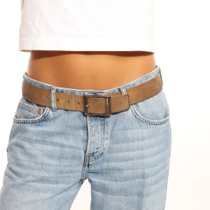 Brunt mockabälte med fyrkantigt spänne - Snyggt brunt bälte i mocka med ett stilrent fyrkantigt spänne. Perfekt för att ge en touch av stil till dina jeans eller andra byxor. Ett måste för garderoben!