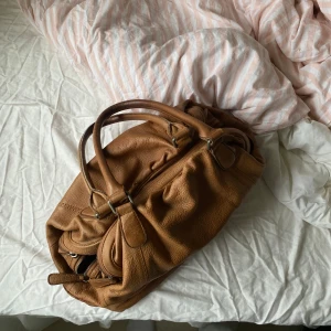 Brun väska i läder - Jättesnygg mellanstor väska i äkta läder från märket Liebeskind. Har 3 separata stora fack med dragkedja så den får verkligen plats med mycket, men är fortfarande lagom stor som axelväska. Insidan och utsidan är rengjord och tvättad