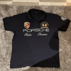 Mörkblå pikétröja från La Martina - Säljer en mörkblå pikétröja från La Martina med Porsche Polo Team-tryck på framsidan. Tröjan är XL med sitter som M