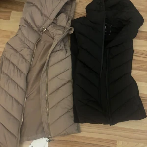 Beige och svart dunväst från Zara - Två snygga västar från Zara i beige och svart. Västarna har en praktisk dragkedja och huva, perfekt för kyligare dagar. Stilren design som passar till många olika outfits. 250 styck!