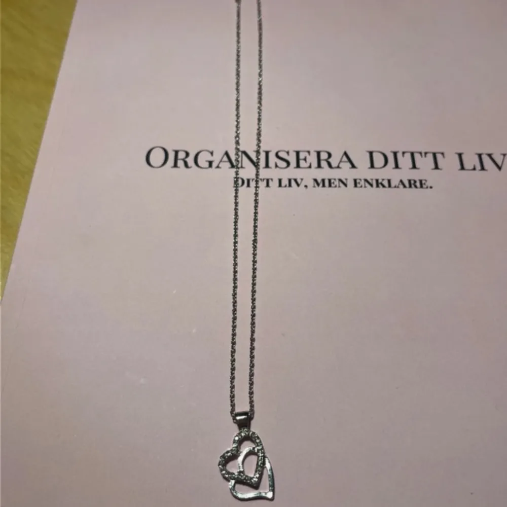 Elegant silverfärgat halsband med ett dubbelt hjärthänge. Hänget har en glittrig detalj som ger en extra touch av stil. Perfekt för att komplettera din look med en romantisk känsla. Aldrig använd. Köpt från ur & Penn. Säljer för 75 kronor.✨. Asusteet.