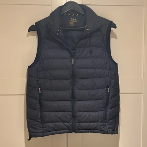 Blå dunväst från Polo Ralph Lauren - Säljer en snygg blå dunväst från Polo Ralph Lauren, som jag tyvärr växt ur. Västen är i väldigt bra skick förutom ett jätte litet ihop limmat håll på ryggen som är laggad så man knappt ser och inge mer med västen än de. Pris kan diskuteras!