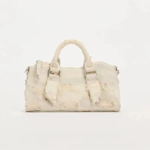 Beige handväska jeans material  - Säljer en unik beige handväska med fransar och slitna detaljer. Väskan har två korta handtag och en dragkedja upptill. Perfekt för att ge din outfit en bohemisk touch.