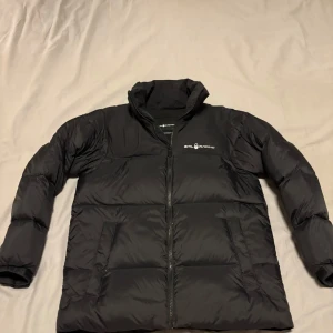 Svart dunjacka från Sail Racing - Säljer en svart dunjacka från Sail Racing. Jackan har en dragkedja framtill och är och märke på bröstet. Skick 10/10. Nästan aldrig använt 