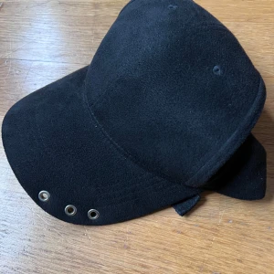 Svart keps i polyester - Snygg svart keps i 100% polyester med tre metallöljetter på skärmen. Perfekt för en stilren look. Tillverkad i Kina.