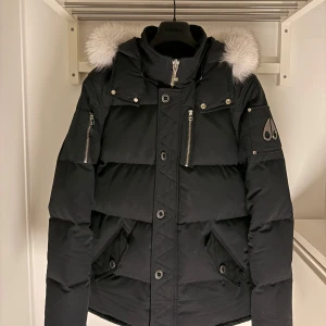 Moose Knuckles Q3 Dunjacka - Säljer Moose Knuckles q3 dunjacka i svart färg med den klassiska vita pälsen på huvan. Jackan har flera dragkedjor och knappar samt den ikoniska moose knuckles loggan på armen. Perfekt för kalla dagar med sin tjocka och varma design. Jackan är såklart autentisk med ett nypris på runt 13999kr, medans mitt Pris är 4490kr (ej hugget i sten). Jackan är knappast änvänd och har inga skador. Det är som sagt i extremt fint skick och 100% felfri. Så hör gärna av er om ni är intresserade! 