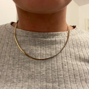 Guldhalsband - Elegant guldhalsband med en tunn, platt design. Halsbandet har en justerbar kedja för att passa olika längder. Perfekt för att lägga till en subtil touch av elegans till din stil.
