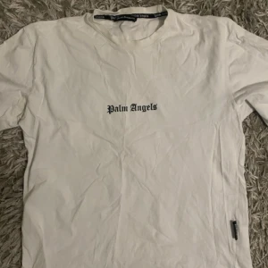 Vit t-shirt från Palm Angels - Säljer en stilren vit t-shirt från Palm Angels med svart text på både fram- och baksidan. T-shirten har en klassisk passform och är kortärmad, perfekt för en avslappnad look.