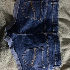 Mörkblå lågmidjade jeansshorts - Snygga mörkblå jeansshorts med klassisk design och uppvikta ben. De har fem fickor och en knappstängning framtill. Perfekta för en avslappnad stil. Dessa shorts är även lågmidjade