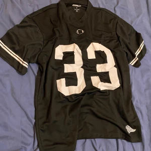 Fotbolls tröja - Säljer en svart sporttröja från New Garments/lager157 med nummer 33 tryckt på framsidan. Tröjan har korta ärmar med vita ränder och är tillverkad i 100% polyester. Perfekt för sportiga aktiviteter eller som en casual look.Storlek S men sitter lite oversized.