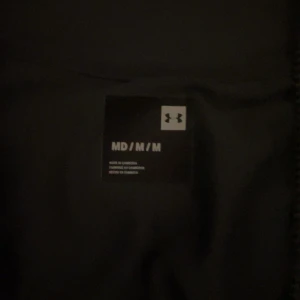 Svart träningsjacka från Under Armour - Säljer en svart träningsjacka från Under Armour. Jackan har en dragkedja framtill och långa ärmar. Perfekt för träning och andra aktiviteter. Den är stilren med en diskret logga på bröstet.
