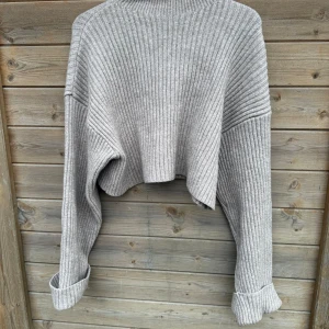 Grå ribbad polotröja från Zara - Säljer en stilren grå ribbad polotröja från Zara. Tröjan har en croppad design med långa ärmar och en hög krage. Perfekt för kyligare dagar och enkel att matcha med olika outfits.