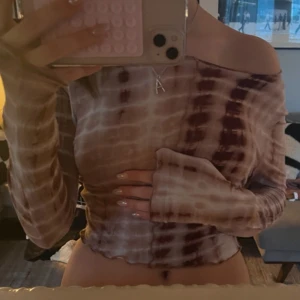 Brun och vit tie-dye topp - Säljer en trendig brun och vit tie-dye topp med långa ärmar. Toppen har en offshoulder-design och är tillverkad i ett mjukt och bekvämt material. Perfekt för en avslappnad stil.
