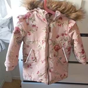 Rosa blommig vinterjacka med fuskpäls - I mycket fint skick förutom det med reflexen annars är den i mycket fint skick storlek 86 satt bara någon storlek för fanns ej storlek 86 i barnstorlek 