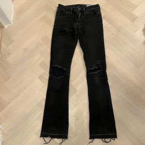 Svarta jeans med slitningar - Säljer ett par svarta jeans med coola slitningar på knäna och fransiga benslut. De har en tight passform och är perfekta för en avslappnad men stilren look. Passar både till vardags och fest. Man kan även sy dessa till boot cut!