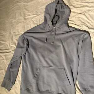 Grå hoodie - Säljer en stilren grå hoodie i mycket bra skick. Den har en klassisk design med en stor ficka framtill och justerbar huva. Perfekt för både vardag och mysiga stunder. Passar till alla säsonger!
