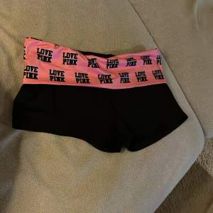 Säljer ett par svarta shorts med en bred rosa resår i midjan där det står 'LOVE PINK' i svart text. Perfekta för en avslappnad dag eller träning. De är i bra skick och superbekväma att ha på sig. Passar perfekt för sommarens alla aktiviteter!