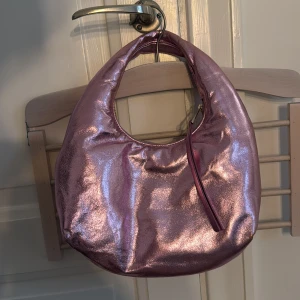 Rosa glittrig axelväska - Säljer en superfin (SLUTSÅLD) 100% rosa_metallic axelväska från & Other Stories. Väskan har en rund form och är gjord av 100% läder med en dragkedja upptill. Perfekt för att liva upp vilken outfit som helst! Ej använd, hel och ren. Pågrund av metallic färgat läder har den lite struktur vilket syns på bilderna. 