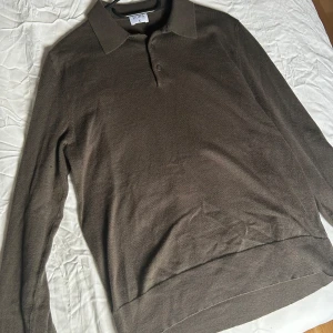 Mörk grön pikétröja från Filippa K - Säljer en stilren brun pikétröja från Filippa K i mycket bra skick. Tröjan har långa ärmar och knappar framtill. Perfekt för både vardag och lite finare tillfällen. Passar bra till höst och vår.