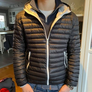 Svart pufferjacka från Colmar - Säljer en snygg svart pufferjacka från Colmar i mycket bra skick. Perfekt för höst och vår men funkar även under vinter, med en stilren design och bekväm passform. Huvan ger extra skydd mot väder och vind. Passar både till vardags och lite finare tillfällen. Kille på bilden är 177cm lång. Kan gå ner i pris vid snabb affär! Hör av er vid frågor.