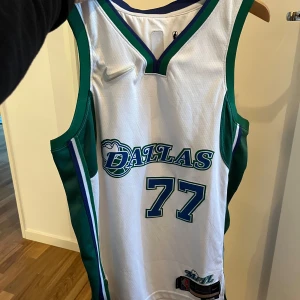 NBA tröja Dallas Mavericks  #77 Luka Doncic  - Säljer en vit basketlinne från Nike med gröna och blå detaljer. Den har nummer 77 och texten 'Dallas' på framsidan samt 'Dončić' på baksidan. Perfekt för basketfans eller som en cool sportig look. 🏀 R Tröja!! 