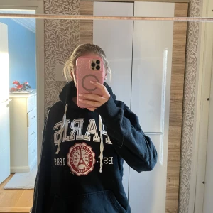 Svart hoodie från Air de Paris - Säljer en svart hoodie från Air de Paris (köpt i paris) i storlek S. Den har en stor text 'PARIS' på framsidan och en cool emblem under. Perfekt för höst och vinter med sin mysiga känsla. Huvan har vita snören och tröjan har en klassisk känguruficka. Passar perfekt för en avslappnad stil!