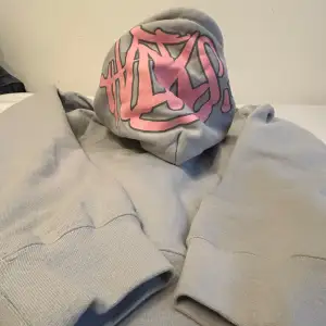 Säljer en syna world grå hoodie med ett coolt rosa tryck på huvan. Den har rosa snören som matchar trycket och ger en extra pop av färg. Perfekt för en avslappnad stil och passar bra till både jeans och mjukisbyxor. Superbekväm och perfekt för kyliga dagar!