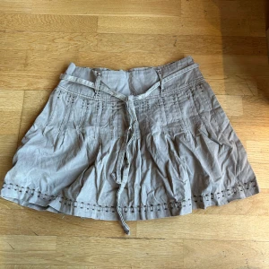 Beige kjol Vero Moda - Säljer en superfin beige kjol från Vero Moda. Den har en söt knytning i midjan och dekorativa sömmar som ger en unik look. Perfekt för både vardag och fest! Köpt second hand men aldrig använd av mig pga den är för stor 🤍