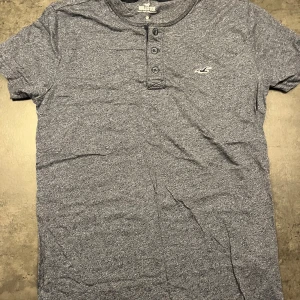 Blå t-shirt från Hollister - Säljer en snygg blå t-shirt från Hollister i bra skick. Blå vit prickigt mönster som på bilderna. Den har en knappdetalj vid halsen och är kortärmad. Perfekt för en avslappnad stil eller vardagsbruk. Passar bra till jeans eller shorts! Nypris 200:-