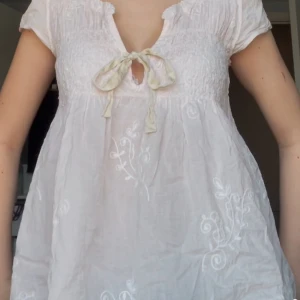 Vit blus med broderade detaljer - Säljer en söt vit blus med fina broderade blommönster. Blusen har korta ärmar och en knytning framtill som ger en romantisk touch. Perfekt för vår och sommar! 🌸