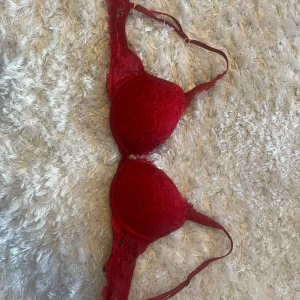 Röd spets-bh push up - Säljer en snygg röd bh med spetsdetaljer. Den har justerbara axelband och en bekväm passform. Perfekt för att känna sig extra fin till vardags eller fest. Använd ett fåtal gånger, så den är i bra skick.