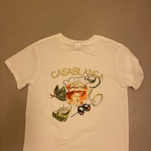 Vit t-shirt från Casablanca - Säljer en vit t-shirt från Casablanca i mycket bra skick. Den har ett coolt tryck på baksidan med en drink och texten 'Casablanca'. Perfekt för sommaren och avslappnade dagar. Normal passform och kortärmad. (Tröjan är Storlek M) men passar ändå L eftersom tröjan är en Oversize tröja