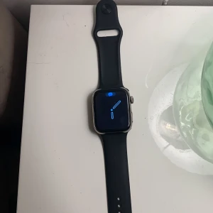 Svart smartklocka med aktivitetsfunktioner - Säljer en svart smartklocka i mycket bra skick. Den har en stilren design med en rektangulär skärm och svart armband. Perfekt för träning med funktioner som pulsmätning och spel. Klockan är idealisk för både vardag och aktivitet.